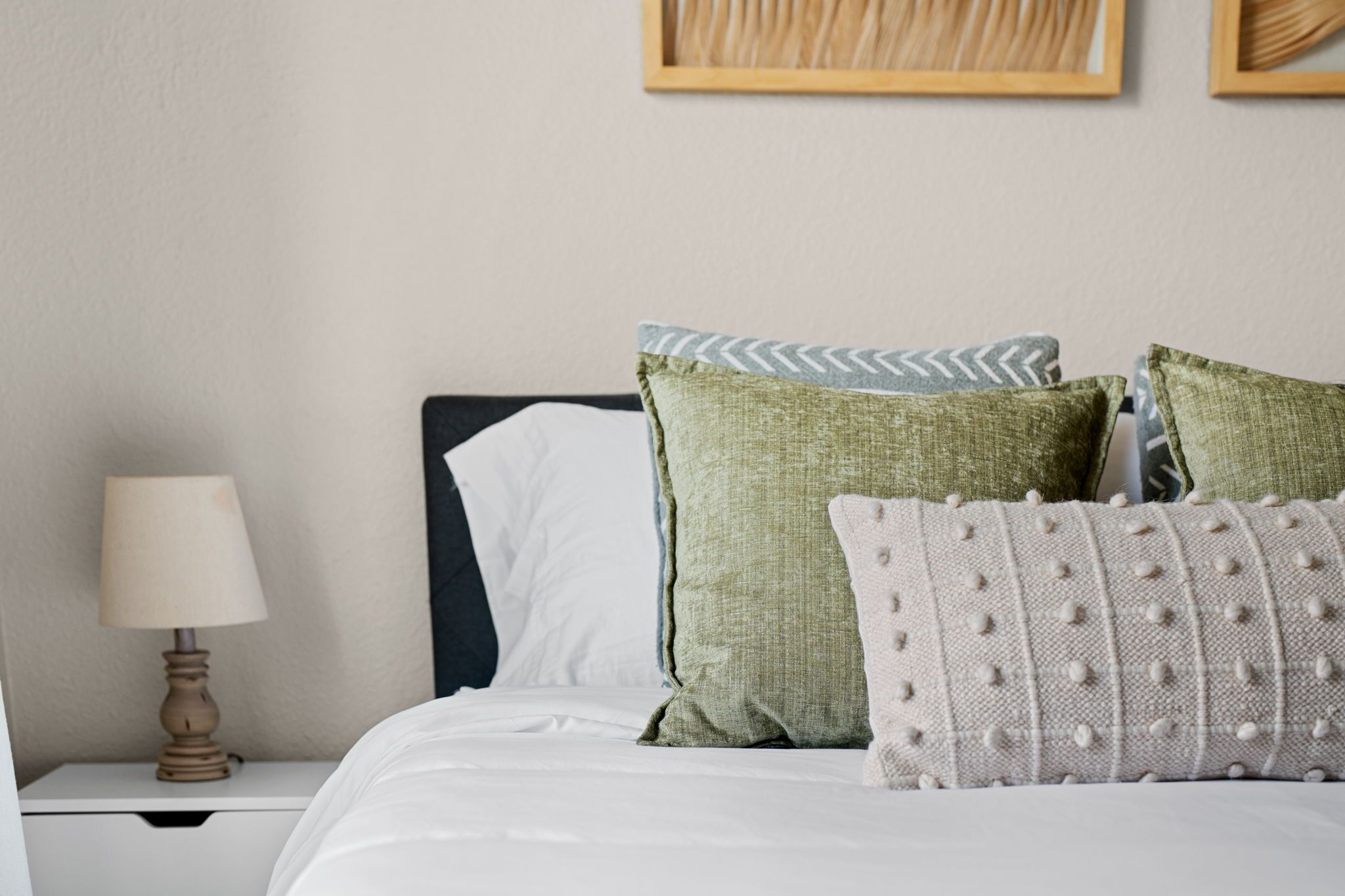 Una cama bien hecha con sábanas blancas y tres almohadas de diferentes diseños.