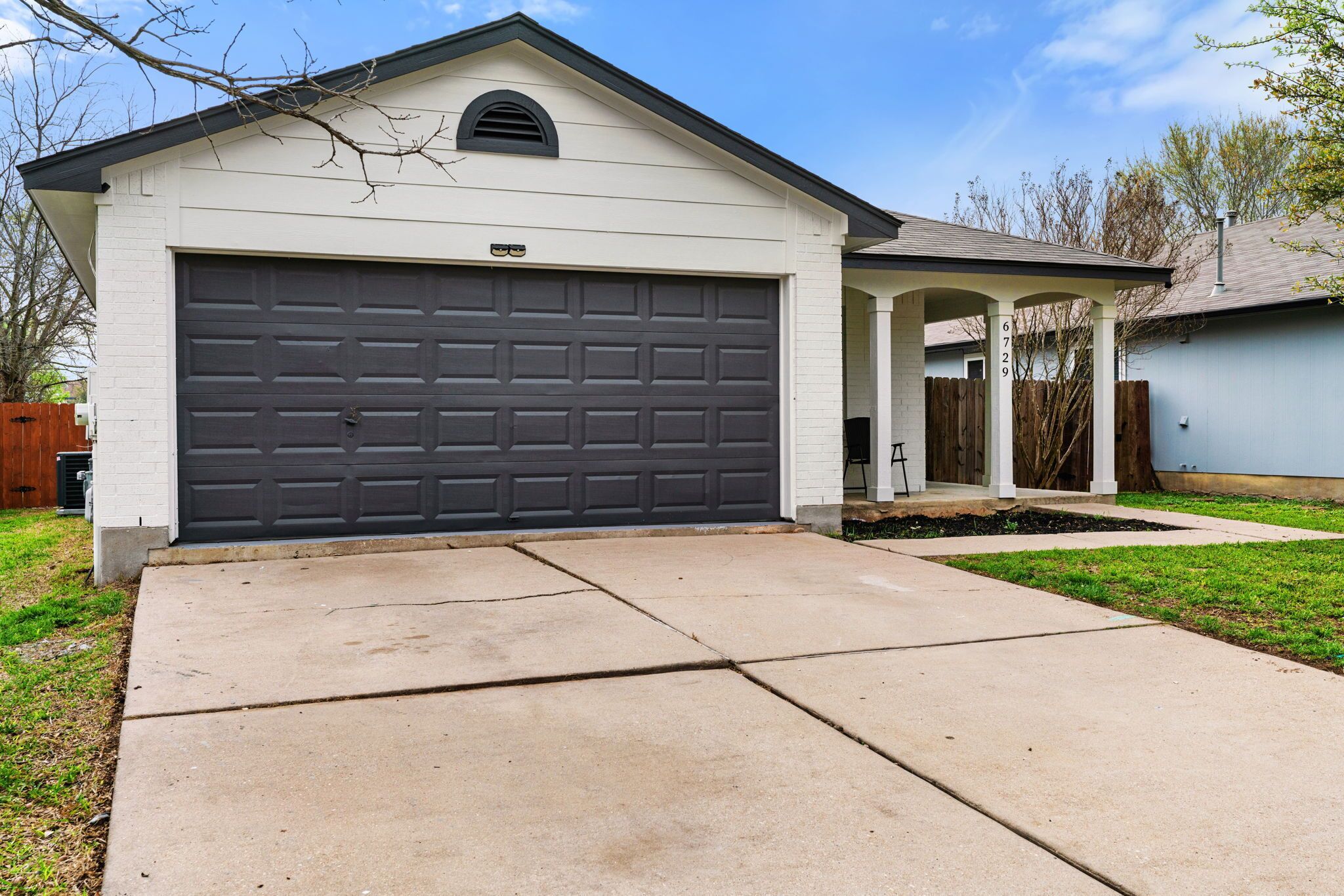 A single-story house with a dark garage door, a small porch, and a visible address number.