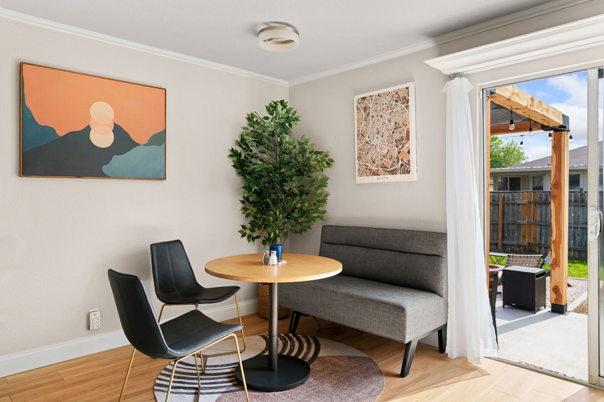 Una sala de estar moderna con un sofá gris, dos sillas negras, una mesa redonda de madera y una planta verde grande.