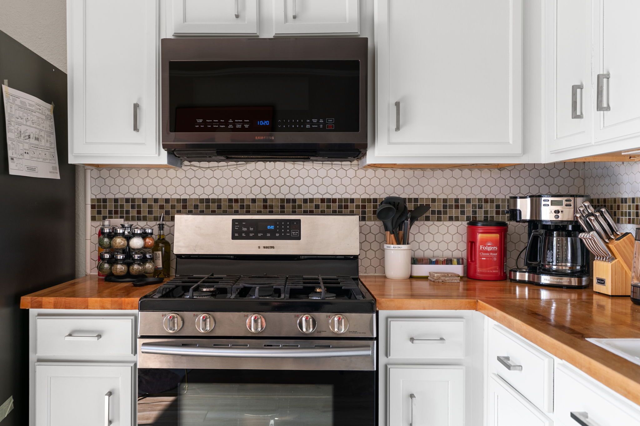 A kitchen with white cabinets, a stainless steel stove, a microwave, and a coffee maker.