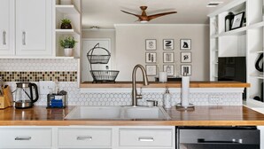 A modern kitchen with white cabinetry, a wooden countertop, a built-in sink, a ceiling fan, and a backsplash with hexagonal tiles. - Solace in South Austin - Game Room (Austin)