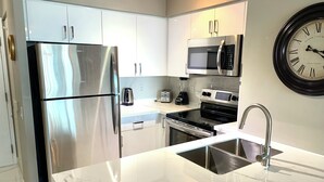 Una cocina moderna con electrodomésticos de acero inoxidable, encimera de mármol y un reloj en la pared.
