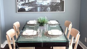 Un comedor con una mesa de vidrio, sillas blancas y una imagen enmarcada de un paisaje urbano en la pared.