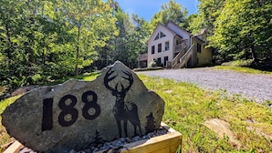 Een stenen paal met het nummer 188 en silhouetten van herten, een huis met veranda en een grindpad in een bebost gebied.