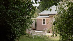 A small house with a metal roof, a garden with a table and chairs, and a fence. - Larsen's Cottage #2: Historic 1880 Home (Mount Victoria)