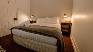 A neatly made bed with a blanket, two bedside lamps, a wooden nightstand, and a door with a handle. - Larsen's Cottage #2: Historic 1880 Home (Mount Victoria)