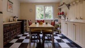 A kitchen with a checkered floor, wooden cabinets, a dining table with chairs, and a window with a view of greenery. - Larsen's Cottage #2: Historic 1880 Home (Mount Victoria)
