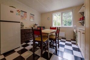 A kitchen with a checkered floor, wooden cabinets, a dining table with chairs, a window with a view, and a clock on the wall.