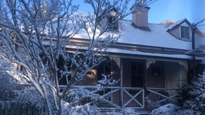 A snow-covered house with a porch, a chimney, and a fence. - Larsen's Cottage #2: Historic 1880 Home (Mount Victoria)