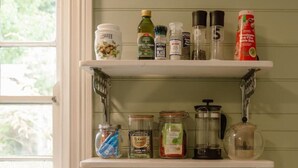 A kitchen with a coffee maker, toaster, and shelves with various kitchen items. - Larsen's Cottage #1: Historic 1880 Home (Mount Victoria)