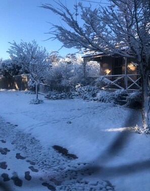 Un espacio exterior cubierto de nieve con una cerca de madera, un edificio pequeño con porche y un sendero.
