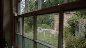 A window view of a garden with a table and chairs, a brick wall, and greenery. - Larsen's Cottage #1: Historic 1880 Home (Mount Victoria)
