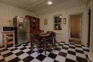 Una cocina con suelo a cuadros, un refrigerador, un microondas, un mueble de madera y una mesa de comedor con sillas.