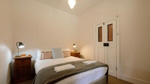 A bedroom with a bed, two bedside tables, a nightstand, a door, and a ceiling light. - Larsen's Cottage #1: Historic 1880 Home (Mount Victoria)