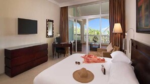 Ein Hotelzimmer mit Bett, Schreibtisch, Stuhl, Fernseher und einem Balkon mit Vorhängen.