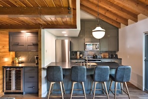 A modern kitchen with a central island, bar stools, and a hanging light fixture.