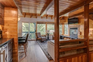 A wooden cabin interior with a dining area, a fireplace, and large windows.