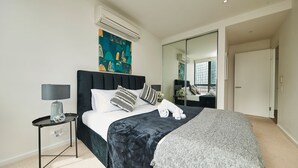 Een moderne slaapkamer met een groot bed, een nachtkastje, een lamp, een schilderij en een spiegel.