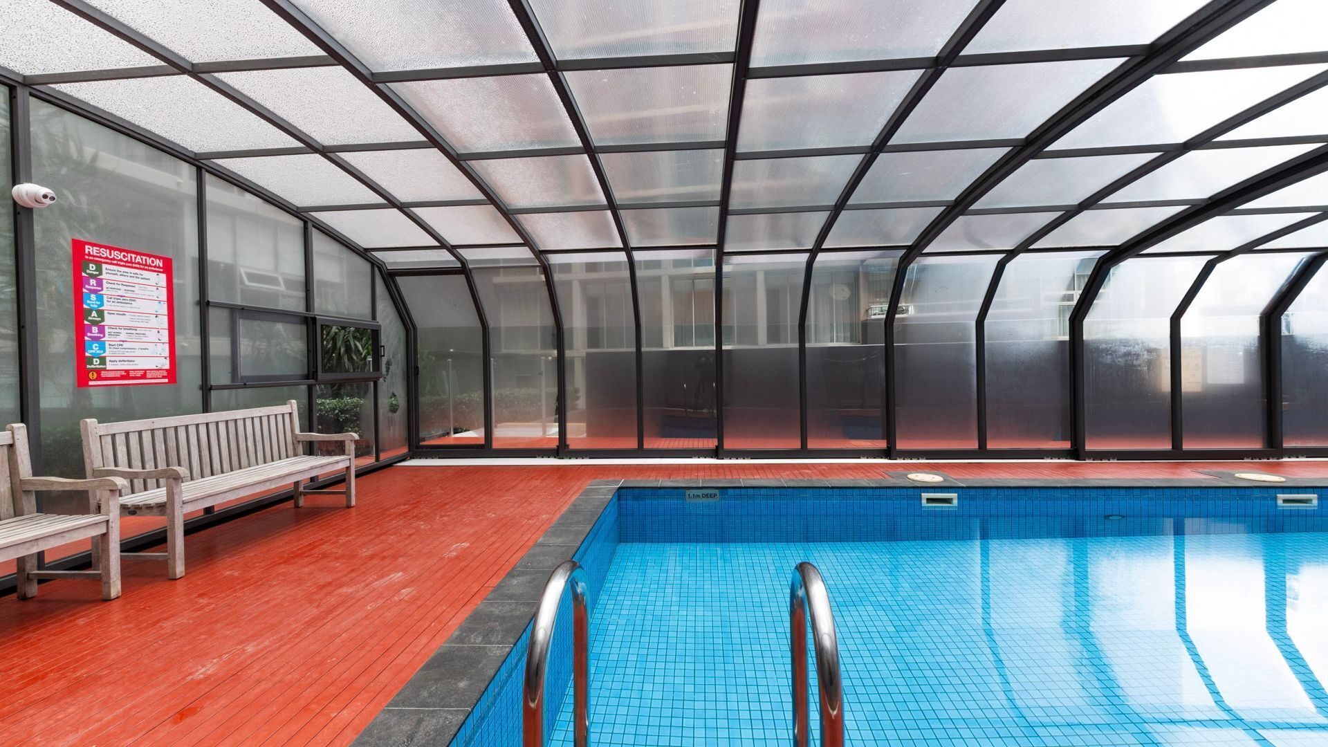 An indoor swimming pool with a clear ceiling, a bench, and a red floor.