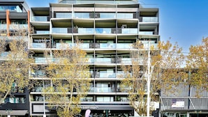 Un immeuble à plusieurs étages doté de balcons, d’une devanture de magasin et d’arbres aux feuilles d’automne.