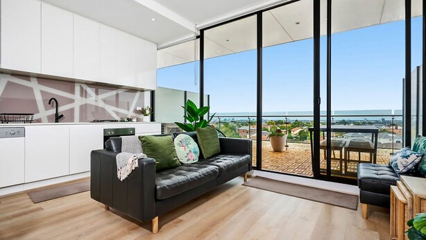 Un apartamento moderno con cocina, un sofá de cuero negro y un balcón con vistas a la ciudad.