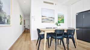Una cocina moderna con un refrigerador negro, una mesa de comedor de madera con sillas negras, y dos cuadros de paisajes en la pared.