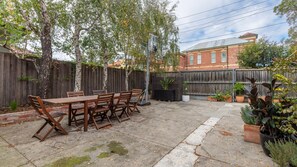 Ein Garten mit einem Holztisch und Stühlen, einem Basketballkorb und einem Ziegelgebäude im Hintergrund.