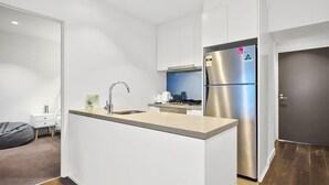 A compact kitchen with a stainless steel refrigerator, a built-in oven, and a sink. - Mr Clarke - Prime Cityscape with Parking (Southbank)