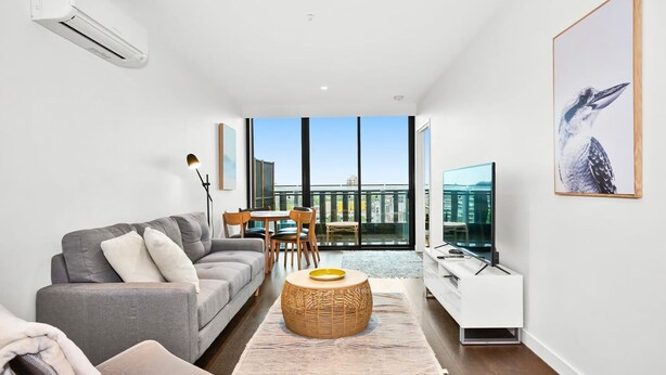 A modern living room with a grey sofa, a small round table, and a TV on a white stand. - Mr Clarke - Prime Cityscape with Parking (Southbank)