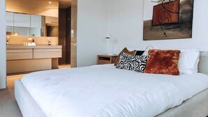 A modern hotel room with a large bed, a bathroom with a vanity, and a painting on the wall.