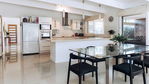 A modern kitchen with a central island, white cabinetry, and a dining area with black chairs.