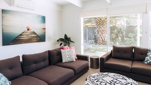 A modern living room with two brown sofas, a coffee table, and a large window with a view of a backyard.