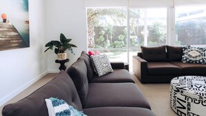 A modern living room with a dark brown sofa, a round ottoman with a patterned cover, and a side table with a potted plant.
