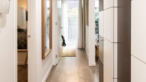 Un couloir étroit doté d’un plancher en bois, de murs blancs et offrant une vue sur un balcon avec une balustrade blanche.
