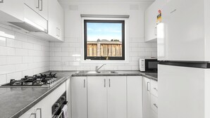A modern kitchen with white cabinets, a gas stove, a microwave, and a window with a view of a wooden fence. - Rosebud Beachfront Haven  Coastal Bliss Four (Capel Sound)