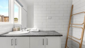 A bathroom with a white sink, a mirror, and a window. There is a wooden ladder leaning against the wall.