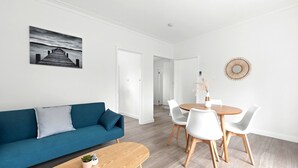 A modern living room with a blue sofa, a wooden coffee table, and a dining area with a round table and white chairs. - Rosebud Beachfront Haven  Coastal Bliss Five (Capel Sound)