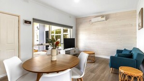 A modern living room with a wooden dining table, white chairs, a blue sofa, and wicker side tables.