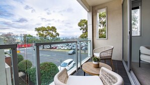 A balcony with wicker furniture, a view of a parking lot, and a framed picture on the wall.