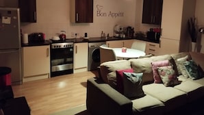 Eine kompakte Küche mit Essbereich, einem Sofa mit Kissen und einer Wand mit einem 'Bon Appetit'-Schild.