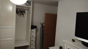 Ein Zimmer mit einem weißen Kleiderschrank, einem kleinen Schreibtisch und einem Fernseher sowie einer Tür.