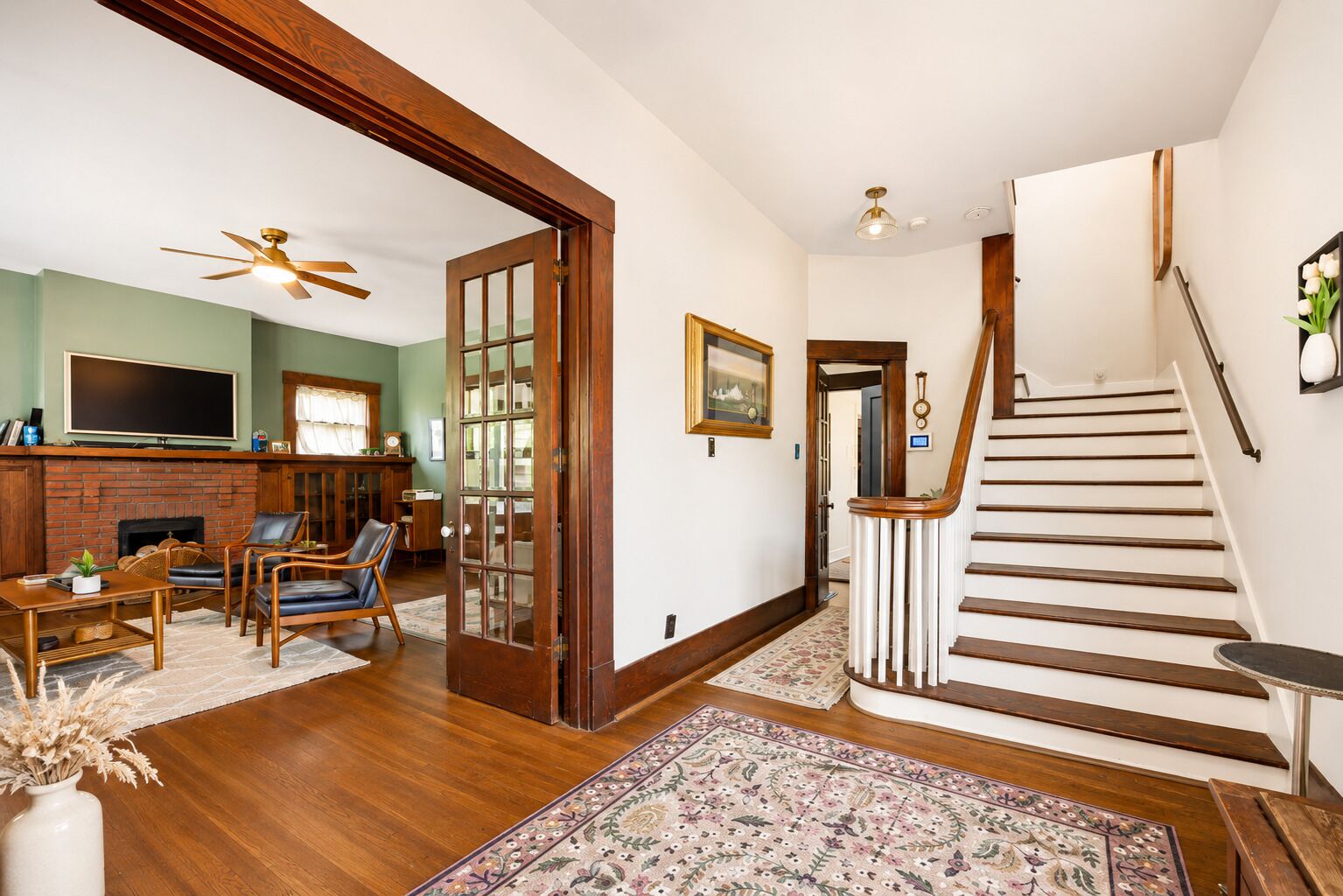 A spacious living room with a fireplace, comfortable seating, a staircase, and a hallway leading to another room.