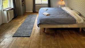 A bedroom with a bed, a radiator, a window, a desk, and a lamp.