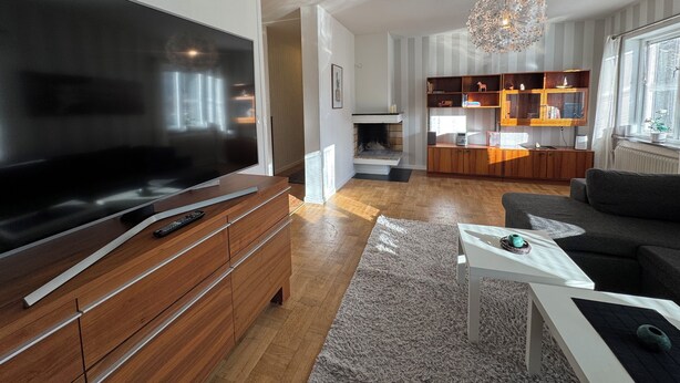A modern living room with a large flat-screen TV, wooden furniture, a white coffee table, and a fireplace.