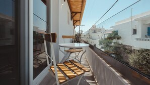 A balcony with a wooden table and chairs, a glass door, and a view of the neighborhood. - Tesoro Elegant escapes-suites (Naxos)