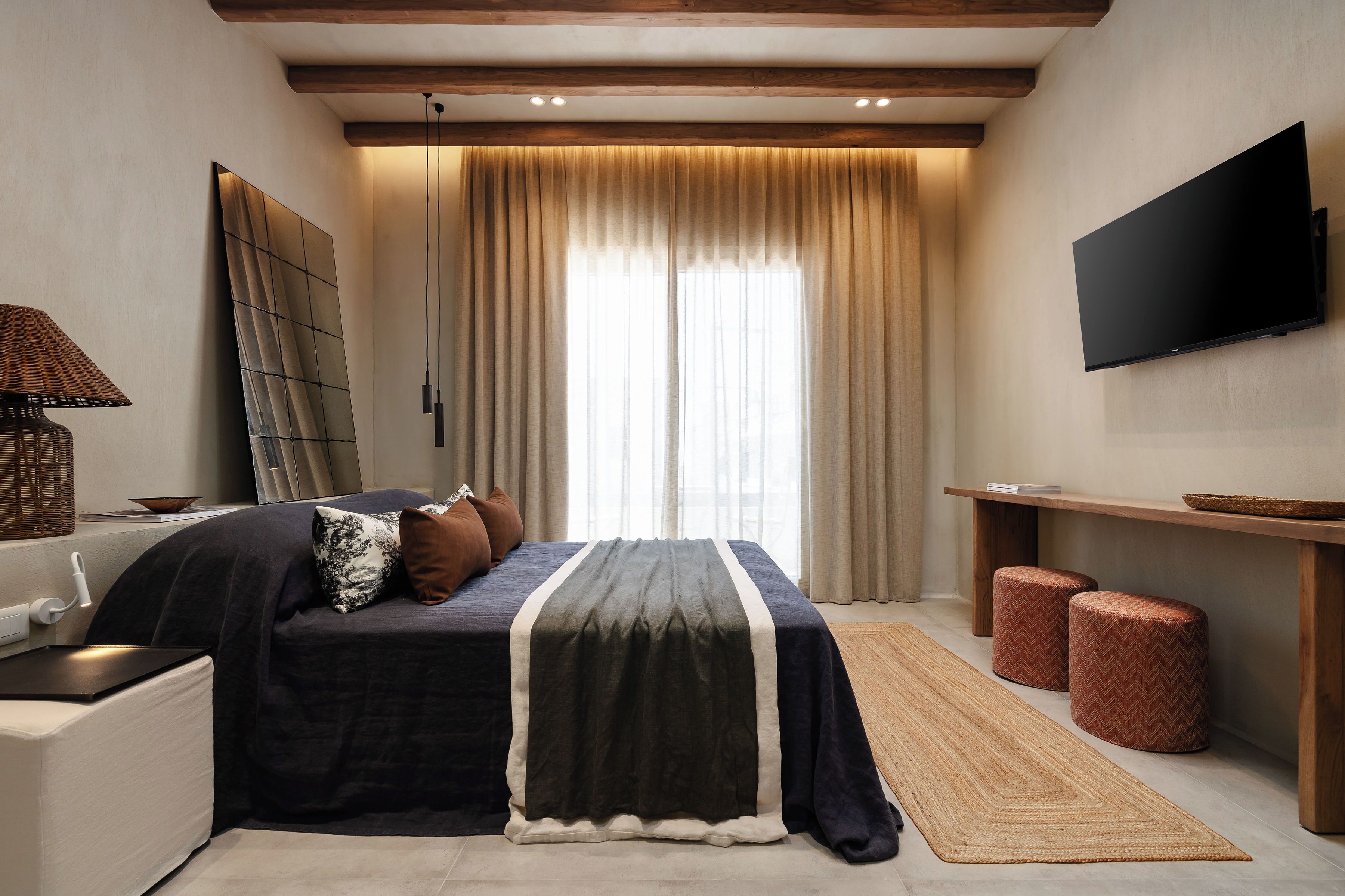 Een moderne slaapkamer met een bed, nachtkastje, lamp, televisie en een groot raam met gordijnen.
