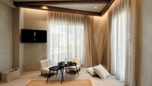 A modern living room with a flat-screen TV, a sofa, a coffee table, and a large window with sheer curtains. - Tesoro Elegant escapes-suites (Naxos)
