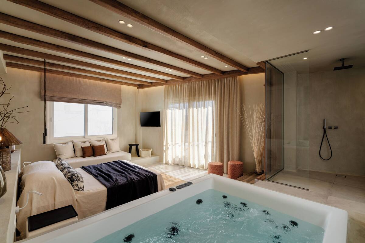 A modern bedroom with a large bathtub, a glass shower, and a TV on the wall.