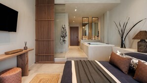 A modern bedroom with a bed, a bedside table, a wooden partition, a bathroom with a bathtub, and a large mirror. - Tesoro Elegant escapes-suites (Naxos)