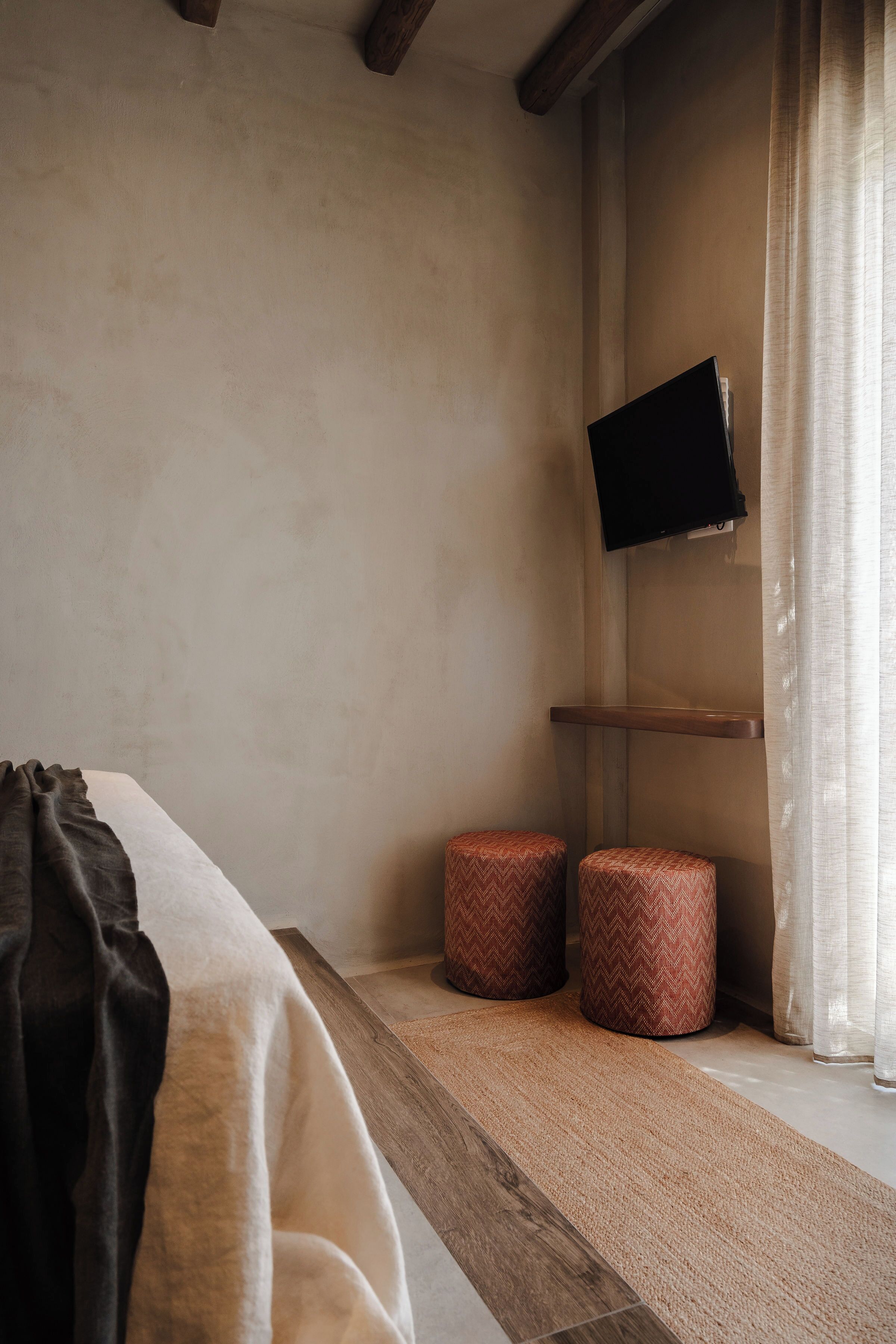 A bedroom with a bed, a mounted TV, and two ottomans.